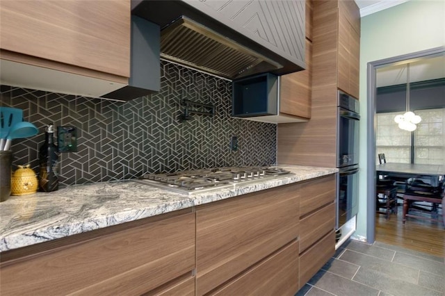 kitchen featuring stainless steel gas stovetop, light stone counters, double oven, backsplash, and premium range hood