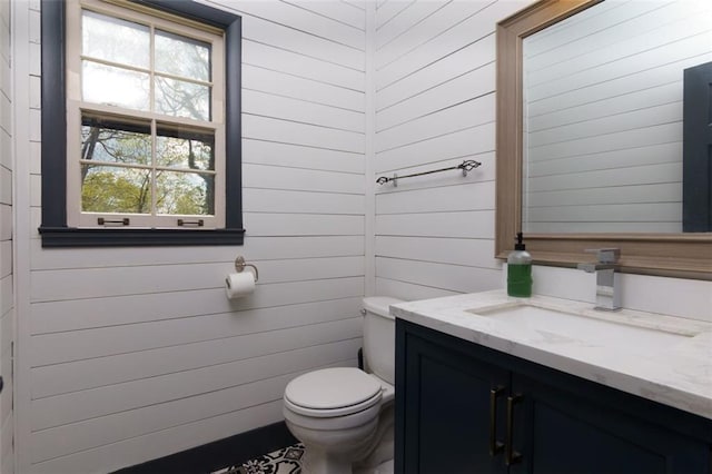 bathroom featuring toilet, wooden walls, and vanity