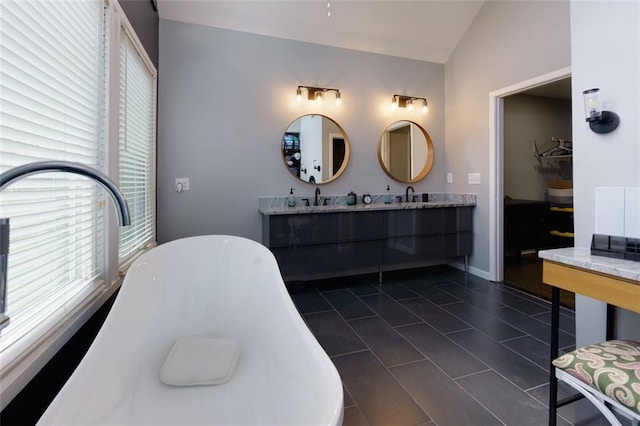 bathroom featuring a freestanding bath, double vanity, lofted ceiling, and a sink
