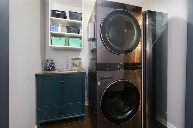 laundry room featuring a sink, stacked washing maching and dryer, cabinet space, baseboards, and dark wood-type flooring