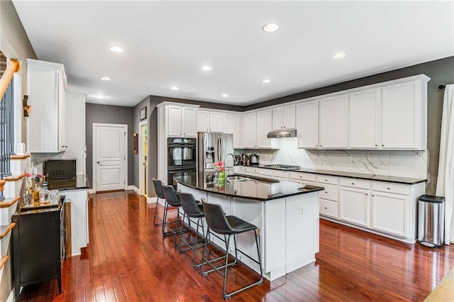 kitchen with a breakfast bar area, dark wood-type flooring, a center island with sink, white cabinets, and appliances with stainless steel finishes