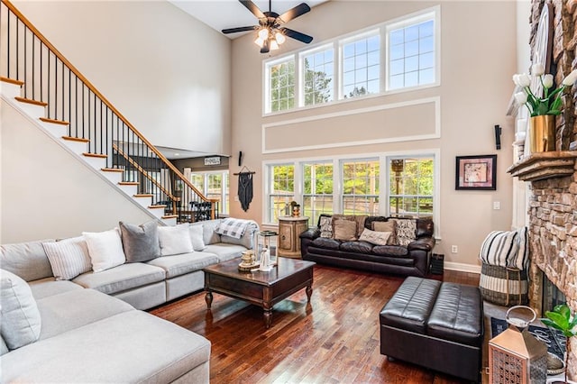 living room with a towering ceiling, dark hardwood / wood-style floors, a fireplace, and ceiling fan