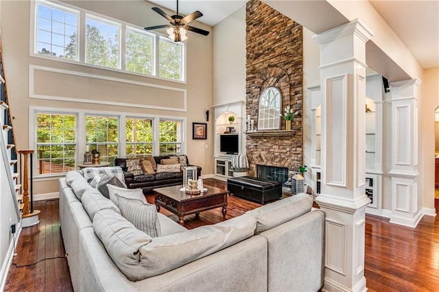 living room featuring a stone fireplace, dark hardwood / wood-style floors, a high ceiling, and ornate columns