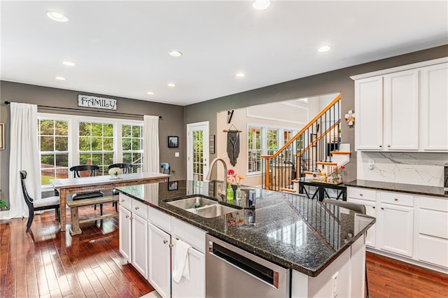 kitchen featuring dishwasher, a kitchen island with sink, dark hardwood / wood-style floors, dark stone countertops, and sink