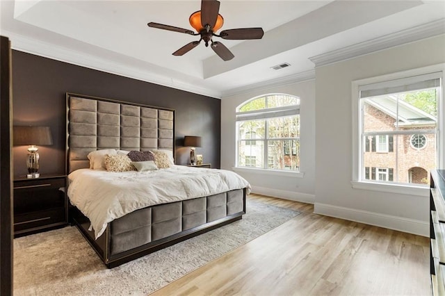 bedroom featuring a tray ceiling, multiple windows, crown molding, wood finished floors, and a ceiling fan