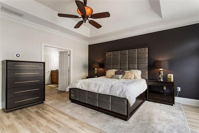 bedroom with a raised ceiling, wood finished floors, ornamental molding, connected bathroom, and ceiling fan