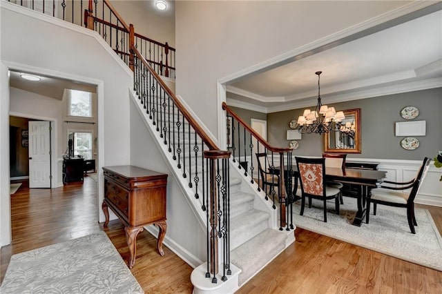 staircase featuring ornamental molding, wood finished floors, a towering ceiling, and an inviting chandelier