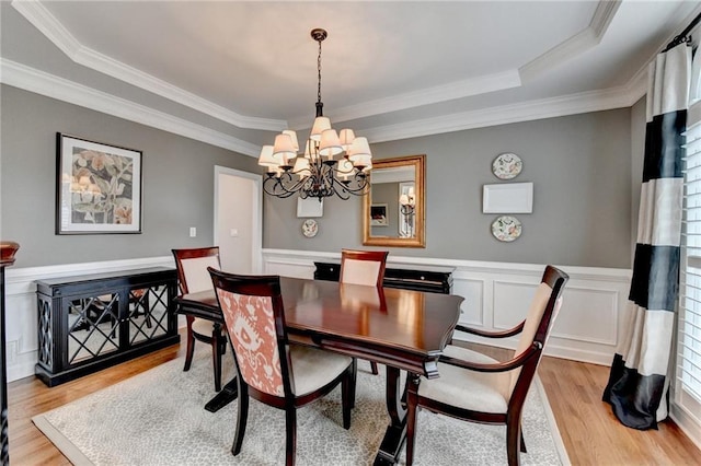 dining area featuring light wood-style floors, wainscoting, ornamental molding, and an inviting chandelier