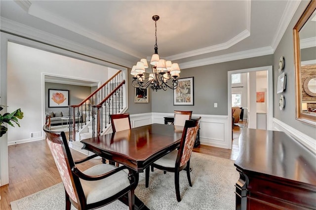 dining area featuring a wainscoted wall, visible vents, ornamental molding, wood finished floors, and stairs