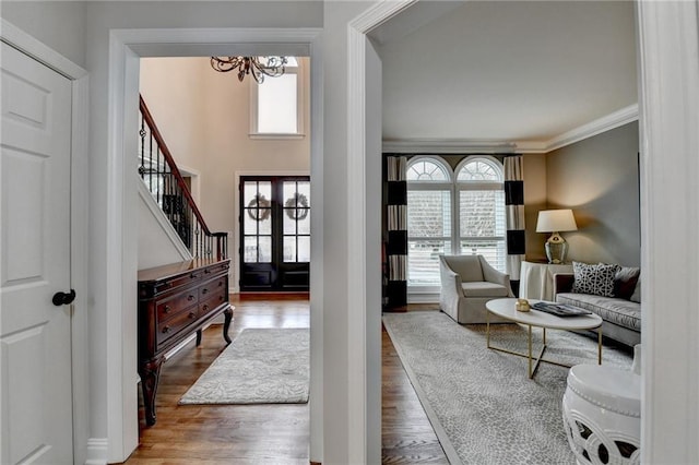 foyer entrance featuring ornamental molding, wood finished floors, an inviting chandelier, and stairs