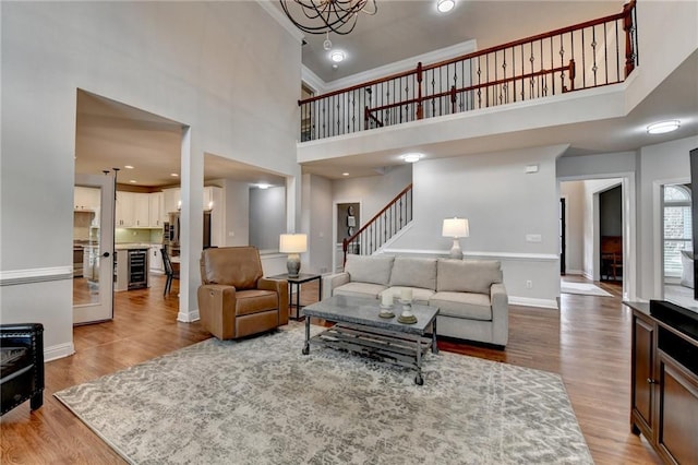 living room featuring baseboards, wood finished floors, a high ceiling, crown molding, and a notable chandelier