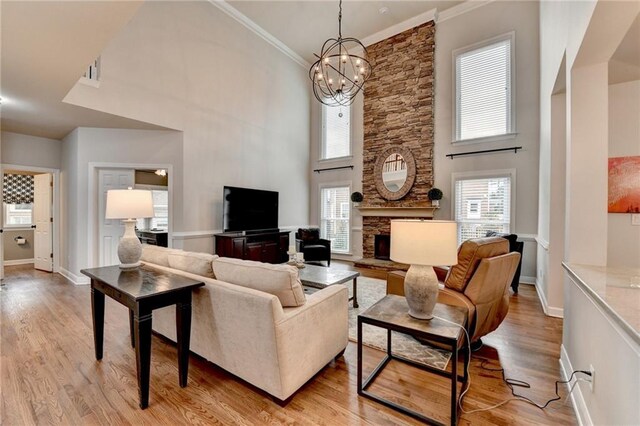 living area featuring light wood-style floors, ornamental molding, a wealth of natural light, and a stone fireplace