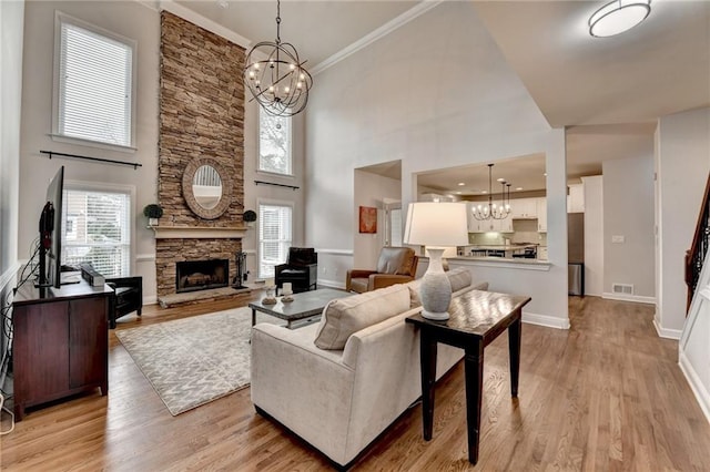 living room featuring a chandelier, a stone fireplace, visible vents, and light wood-style floors