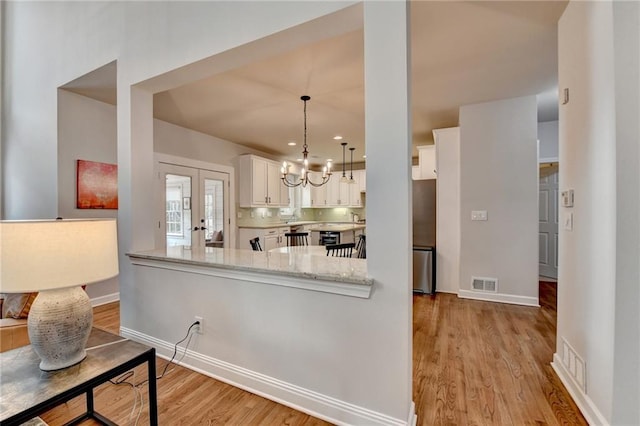 kitchen featuring a chandelier, visible vents, white cabinetry, light wood-type flooring, and light stone countertops