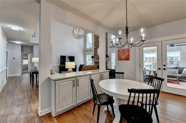 dining room with french doors, light wood-style flooring, baseboards, and an inviting chandelier