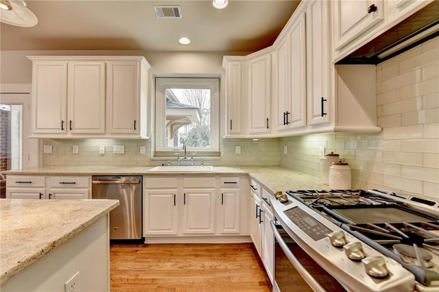 kitchen featuring light wood finished floors, visible vents, white cabinets, stainless steel appliances, and a sink