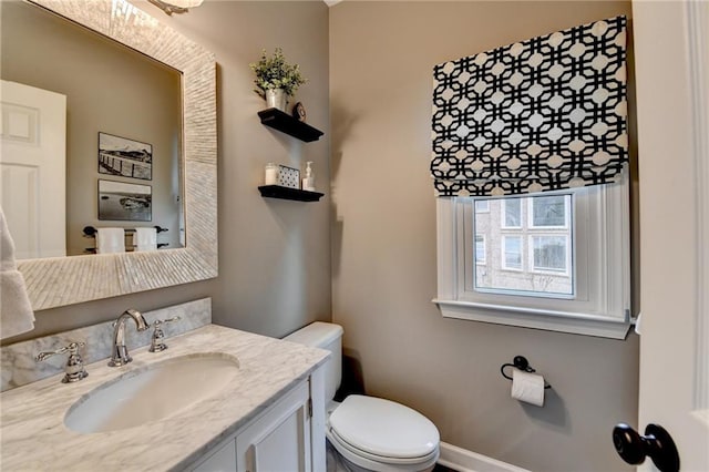 half bathroom featuring toilet, baseboards, and vanity