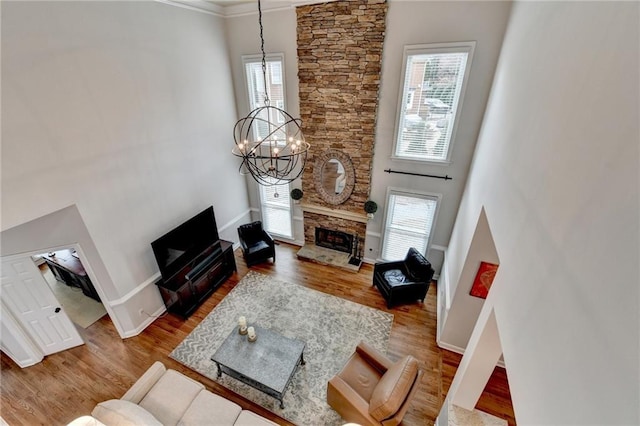 living area featuring a stone fireplace, a notable chandelier, wood finished floors, a towering ceiling, and a healthy amount of sunlight