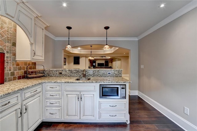 kitchen featuring dark wood-style floors, stainless steel microwave, a peninsula, crown molding, and a sink