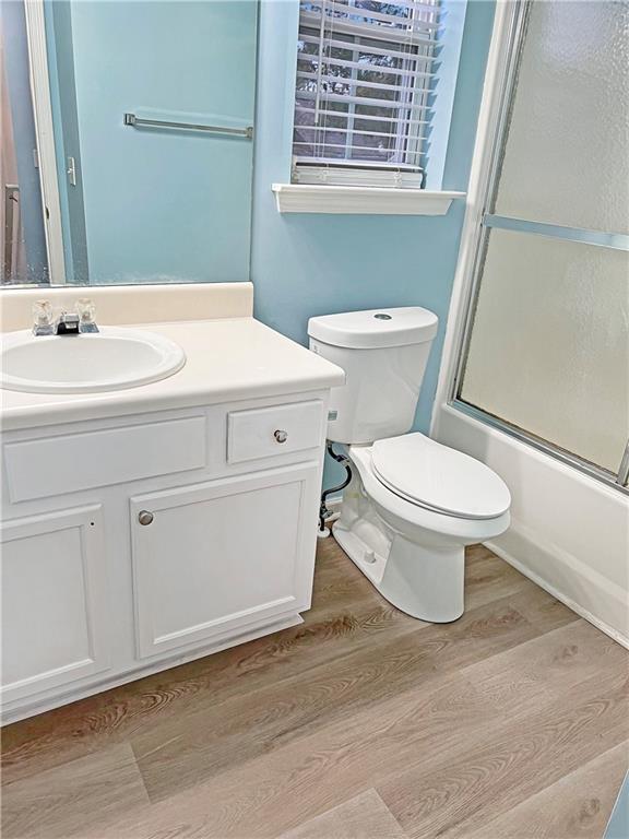 full bathroom with hardwood / wood-style floors, toilet, combined bath / shower with glass door, and vanity