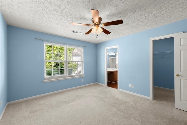 unfurnished bedroom featuring ensuite bathroom, ceiling fan, a spacious closet, light colored carpet, and a closet