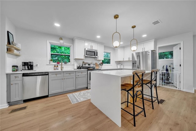 kitchen featuring stainless steel appliances, visible vents, a breakfast bar area, and gray cabinets