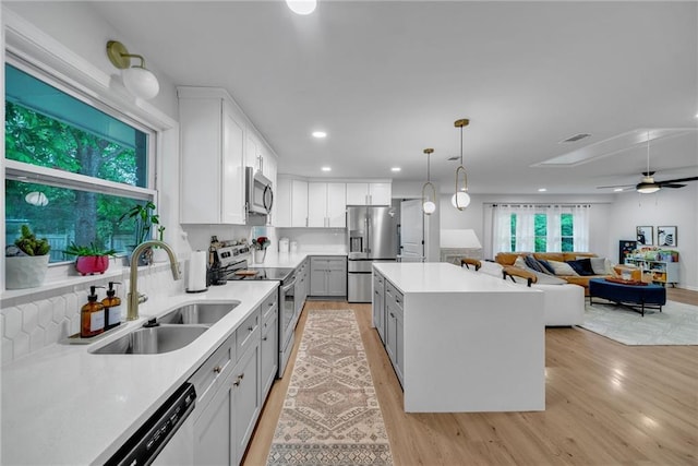 kitchen with gray cabinetry, a center island, light wood-style flooring, appliances with stainless steel finishes, and a sink