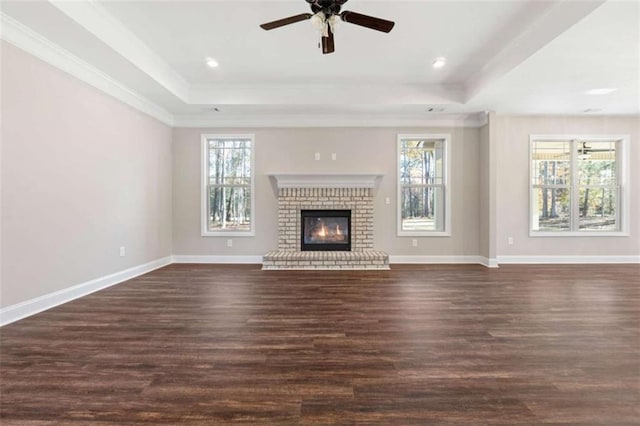 unfurnished living room with crown molding, a raised ceiling, dark wood finished floors, a ceiling fan, and baseboards