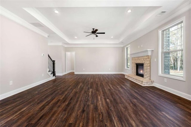 unfurnished living room with stairs, a ceiling fan, wood finished floors, a tray ceiling, and ornamental molding