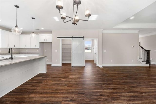 unfurnished living room with dark wood-style floors, baseboards, a notable chandelier, and a barn door