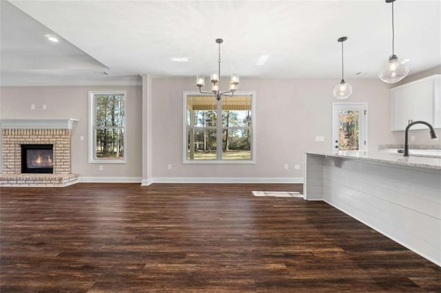 unfurnished living room with baseboards, a notable chandelier, dark wood-style floors, and a fireplace
