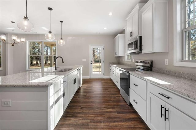 kitchen featuring a center island with sink, dark wood finished floors, a sink, stainless steel appliances, and white cabinetry