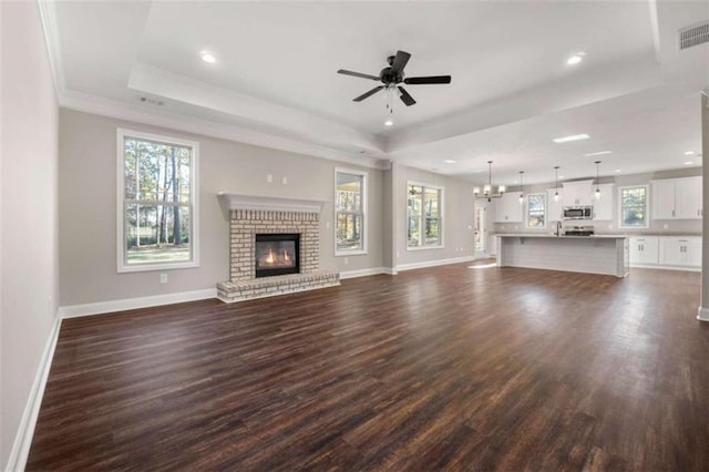 unfurnished living room with visible vents, a fireplace, baseboards, dark wood-type flooring, and a tray ceiling