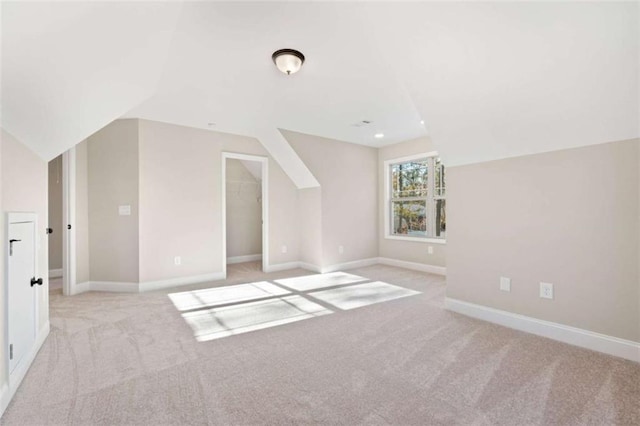 additional living space featuring baseboards, light carpet, and vaulted ceiling