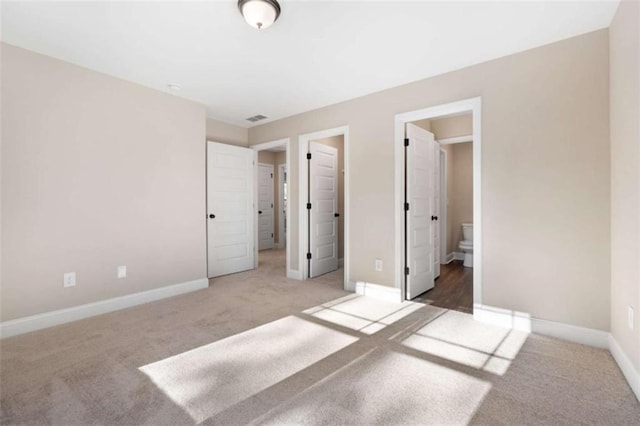 unfurnished bedroom featuring baseboards, carpet flooring, ensuite bath, and visible vents