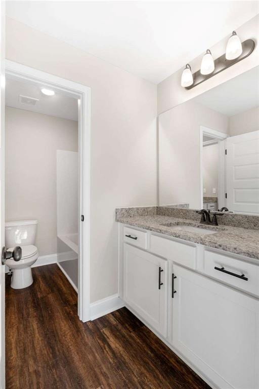 full bath featuring vanity, toilet, baseboards, wood finished floors, and a tub to relax in