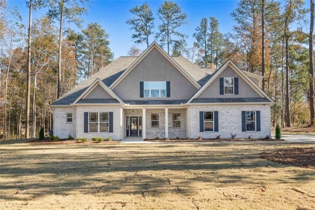 craftsman inspired home with a porch, brick siding, a front yard, and stucco siding