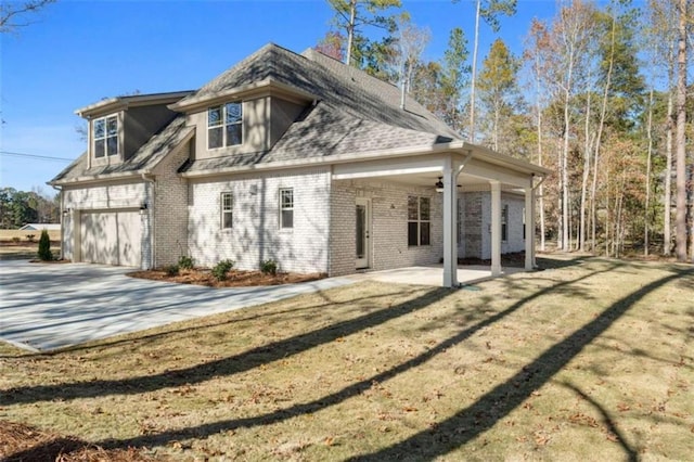 rear view of house with brick siding, a garage, concrete driveway, a patio, and a yard