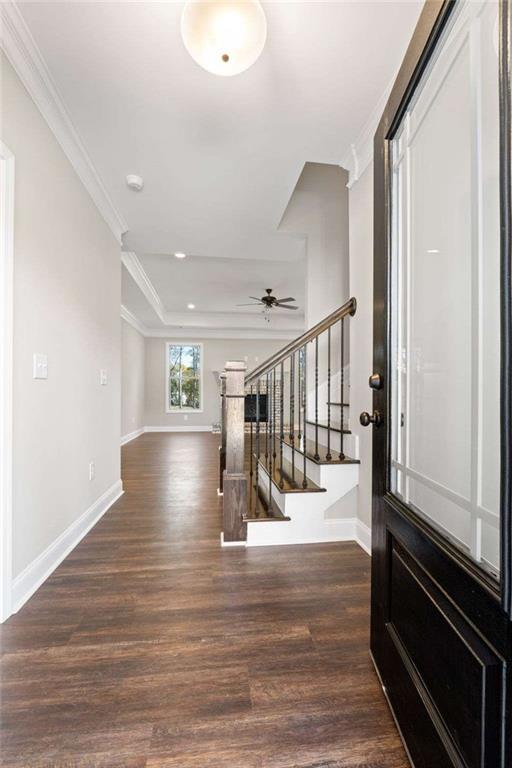 foyer with a ceiling fan, stairway, baseboards, ornamental molding, and dark wood-type flooring