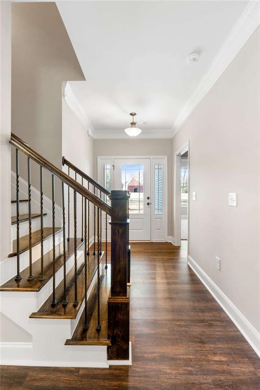 foyer entrance with crown molding, baseboards, wood finished floors, and stairway