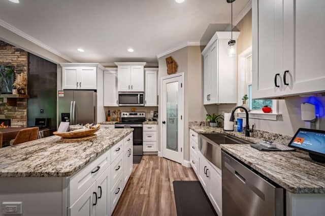 kitchen with a sink, stainless steel appliances, ornamental molding, white cabinetry, and hanging light fixtures