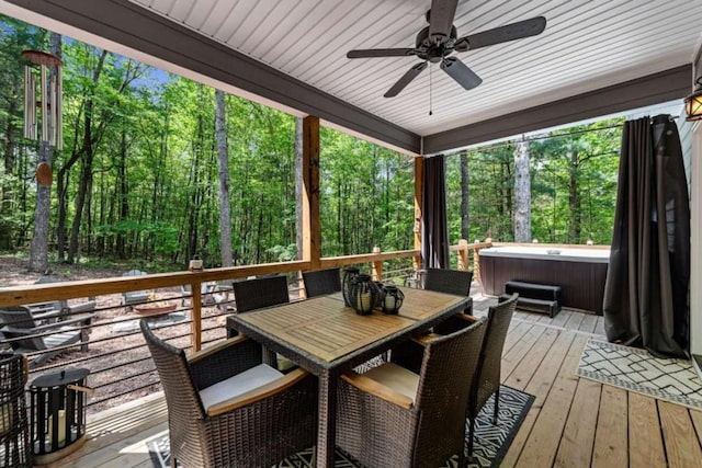 deck featuring a hot tub, a forest view, outdoor dining area, and a ceiling fan