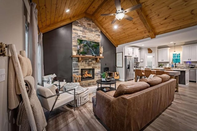 living area featuring wood ceiling, wood finished floors, a ceiling fan, a fireplace, and beamed ceiling