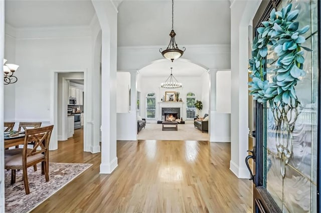 foyer featuring a warm lit fireplace, decorative columns, arched walkways, ornamental molding, and wood finished floors