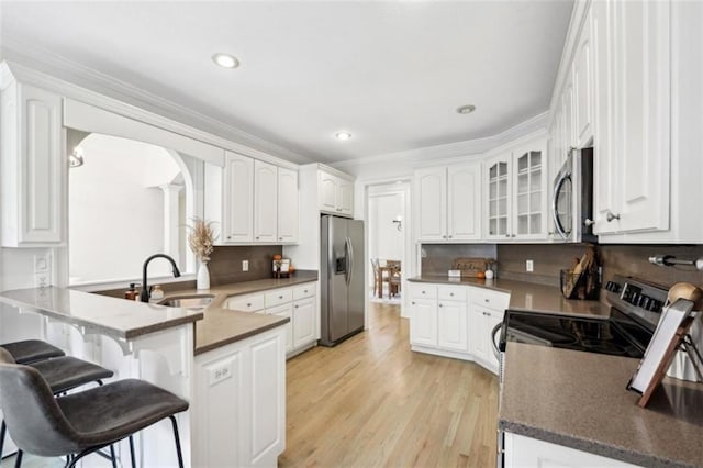 kitchen with white cabinets, a breakfast bar, a peninsula, stainless steel appliances, and a sink