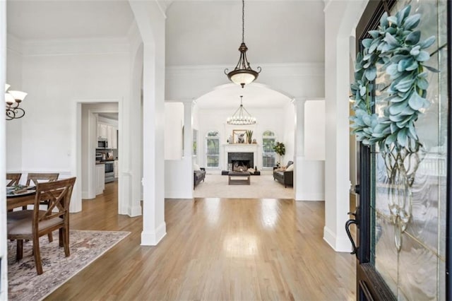 entryway with arched walkways, wood finished floors, crown molding, ornate columns, and a fireplace