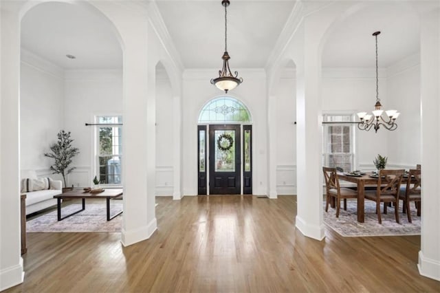 entryway with arched walkways, ornamental molding, wood finished floors, and a decorative wall