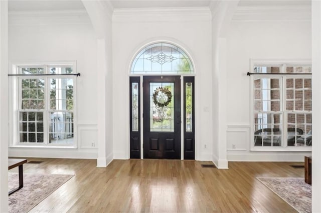 entryway with ornamental molding, beamed ceiling, wood finished floors, and a decorative wall