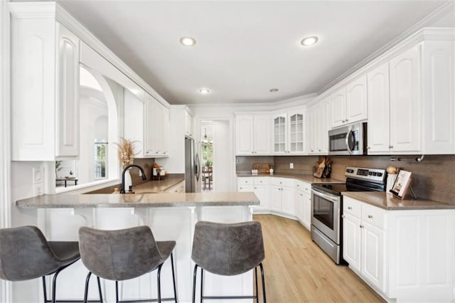 kitchen featuring a peninsula, stainless steel appliances, light wood-type flooring, a kitchen bar, and white cabinetry