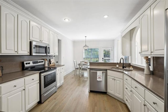 kitchen featuring white cabinets, appliances with stainless steel finishes, decorative light fixtures, light wood-style floors, and a sink